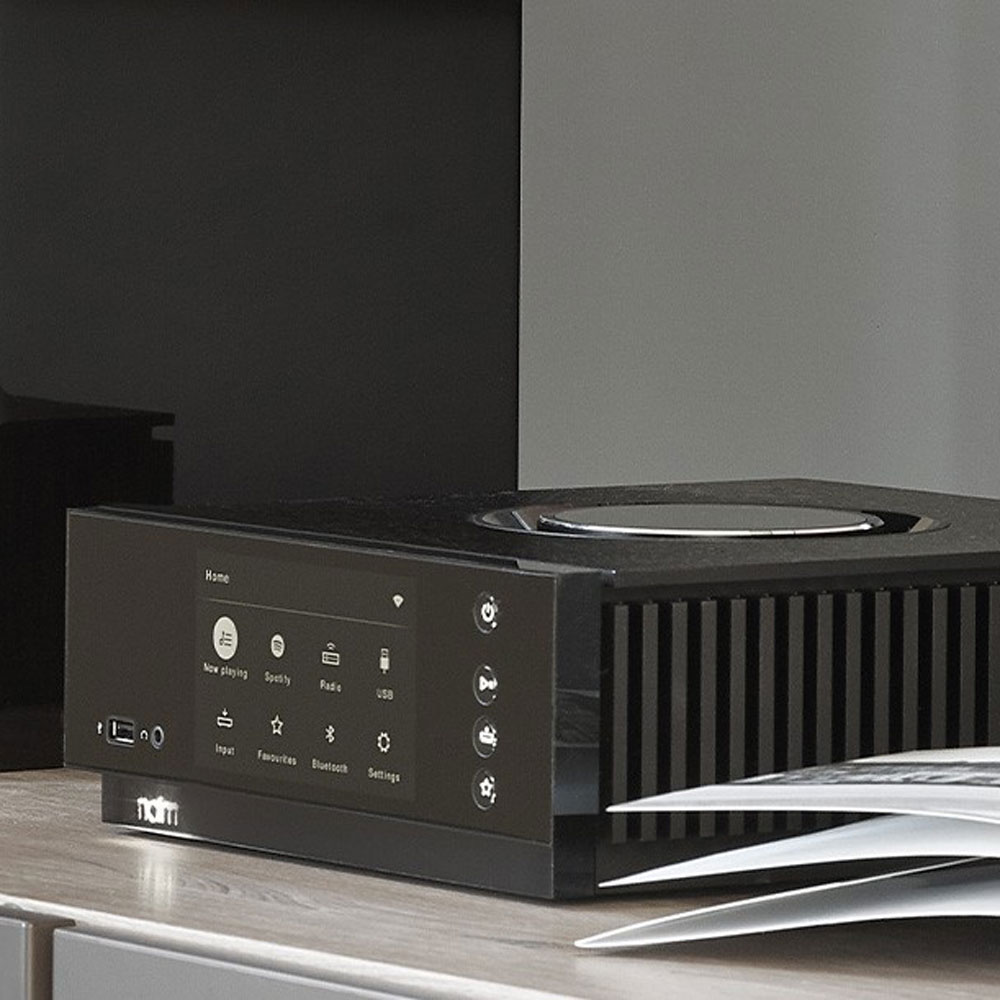 Uniti Atom von naim wie es auf einer Kommode neben einer aufgeschlagenen Zeitschrift steht.